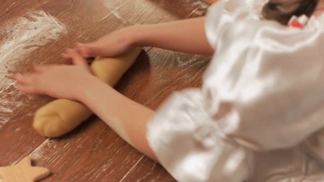 Girl chef rolls the dough by hand on a table, top view.