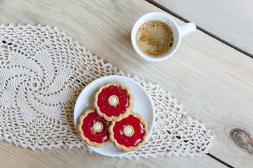Cozy home still life. A cup of coffee and plate with cookies on knitted napkin on light wooden background. Close up.