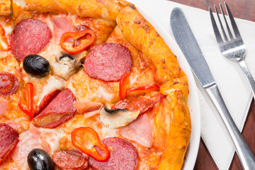 Italian pizza with salami, cheese, mushrooms and olives on a wooden table