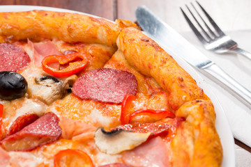 Italian pizza with salami, cheese, mushrooms and olives on a wooden table
