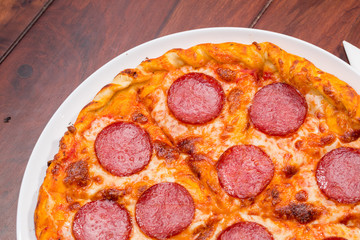 Top view of pizza with salami on a wooden background