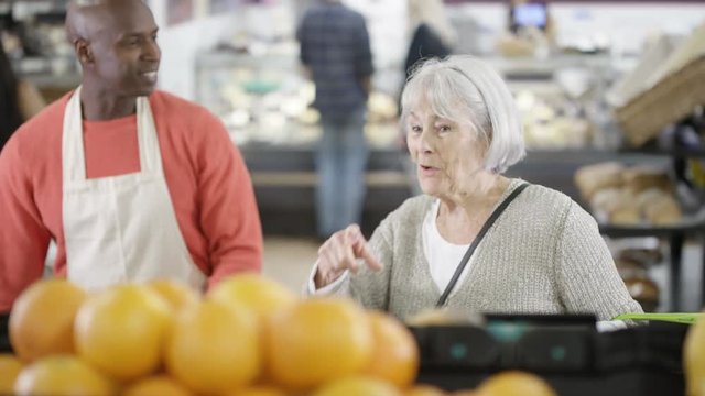  Friendly worker in a supermarket assisting senior lady buying groceries