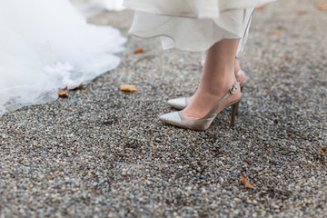 Feet with silver shoes and bridal dress on pebble stone