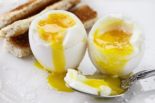 Two soft boiled eggs with toast soldiers over a white plate. Extreme shallow depth of field with selective focus.