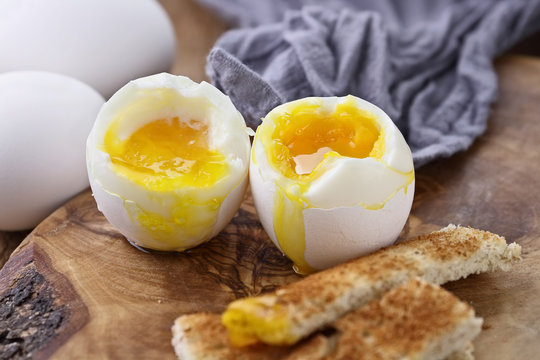 Two soft boiled eggs with toast soldiers against a rustic background. Extreme shallow depth of field with selective focus on yolk.