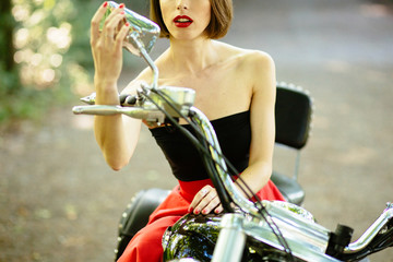 Beautiful girl on motorbike looking in the rearview mirror Attractive woman biker posing near her motorcycle.