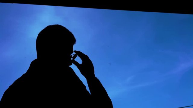 Black silhouette of man removing glasses on blue sky background 4K