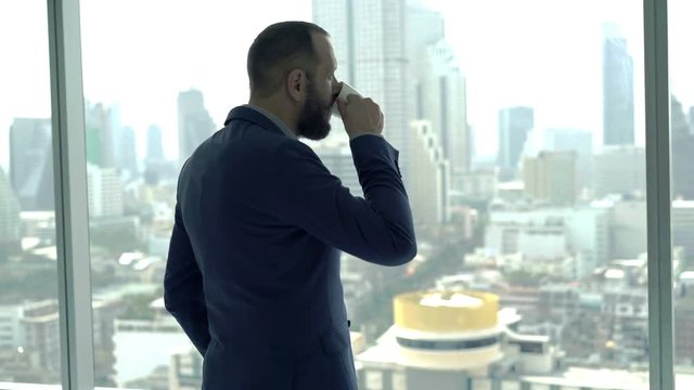 Young businessman drinking coffee and looking through tke window, 4K
