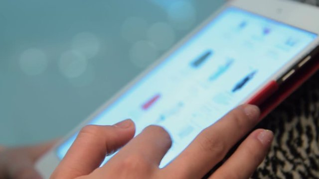Close-up shot of a woman looking at clothing in online store. She scrolling down the site on digital tablet. Easy shopping