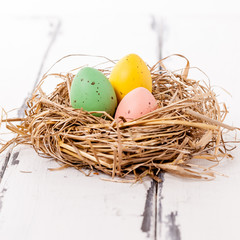 tre pastellfärgade ägg i ett fågelbo