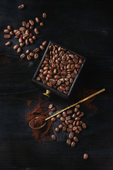 Roasted coffee beans and grind coffee in wood box with spoon over black wooden burnt background. Top view with space.