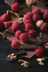 Dark and milk chopping chocolate and chips shavings chopping chocolate with fresh raspberries heap and cracks walnuts over black burnt wooden background. Close up. Chocolate dessert concept
