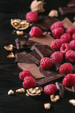Dark and milk chopping chocolate and chips shavings chopping chocolate with fresh raspberries heap and cracks walnuts over black burnt wooden background. Close up. Chocolate dessert concept