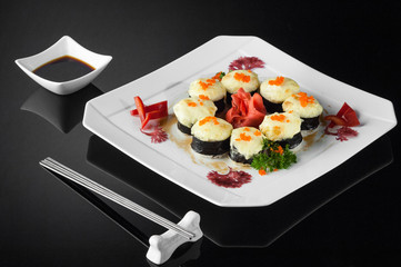 sushi in a white plate with sauce pot and chopsticks on a black background with reflection 