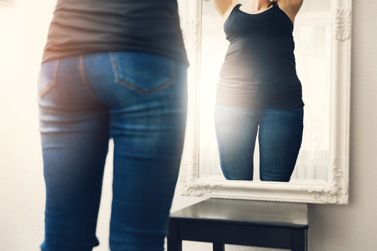 anorexia concept - woman looks at her fat reflection in mirror