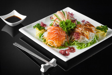 sushi in a white plate with sauce pot and chopsticks on a black background with reflection 