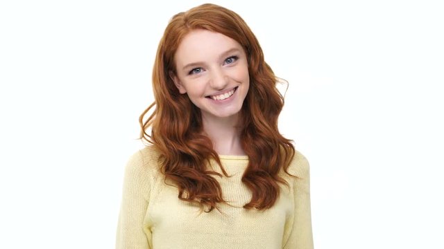 Happy excited young woman with long red hair jumping out with hands raised and making a surprise over white