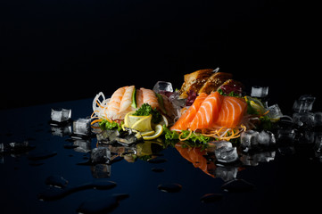 a variety of sushi with pieces of melting ice on a black background with reflection
