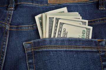 Heap of American money (US currency, USD) in the back pocket of blue jeans with yellow stitching as a symbol of black money earned without taxation 