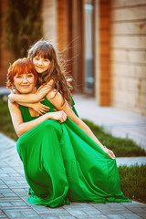 Little girl hugs from behind pretty woman in long green dress