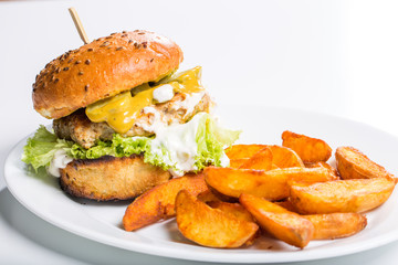 Tasty chicken burger with wedges, on a white plate