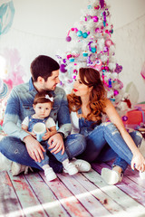 Man and woman look at each other sitting with their daughter before Christmas tree