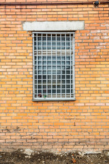 In the brick wall of the building a window with an iron grating