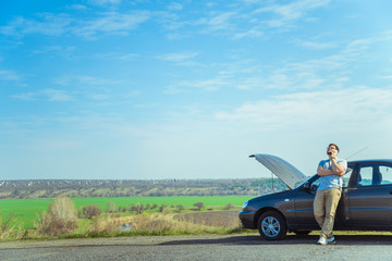 Angry young man waiting a help while sitting near the broken car