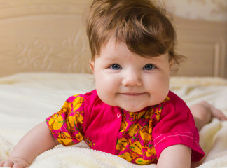 A small child smiling, lying on stomach and looking at the camera.