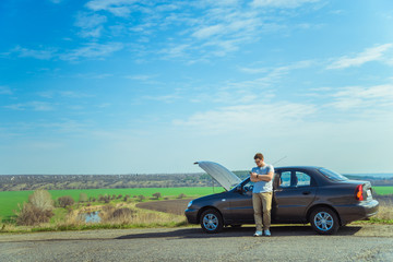 Angry young man waiting a help while sitting near the broken car