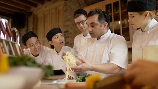  Professional chef talking to happy young trainees in cookery school