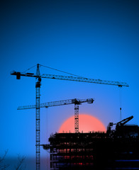 Cranes and building silhouette at dawn.