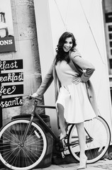 Pretty lady in beige coat sits on the bicycle before a cafe