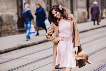 Fototapeta premium Woman in pink dress and beige coat poses on tramways