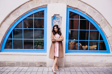 Woman in beige coat stands between blue windows outside