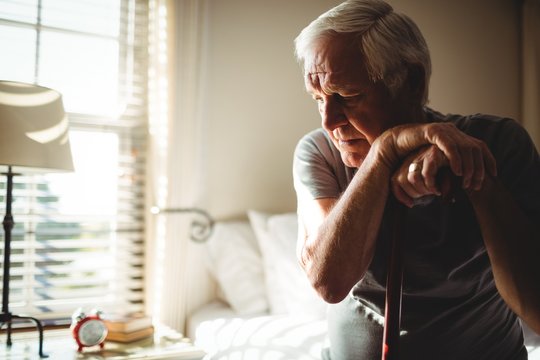 Thoughtful senior man with his walking stick in the bedroom