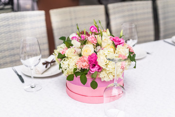 Flower arrangement in a hat box on the table, outdoor. Summer terrace of restaurant