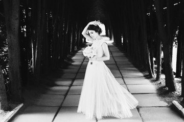 Fototapeta premium Bride in light summer dress holds her hand up posing on path in park