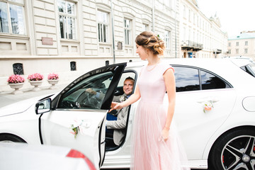 Bride stands before the door while groom sits inside the car - Powered by Adobe