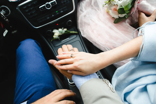 Bride holds her hand on groom's one while he drives a car