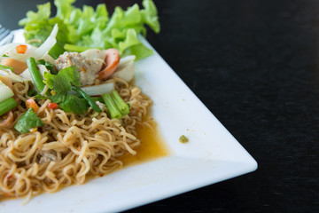 Noodle spicy salad on white dish on black table