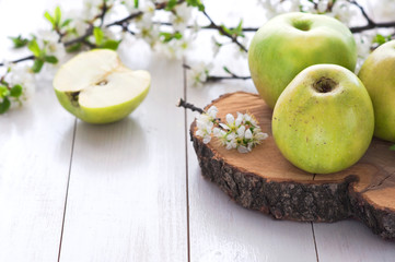 Ripe green apples with spring flowers on a white wooden background.