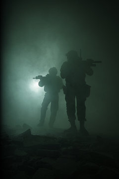 Black silhouettes of pair of soldiers in the smoke haze moving in battle operation. Back light