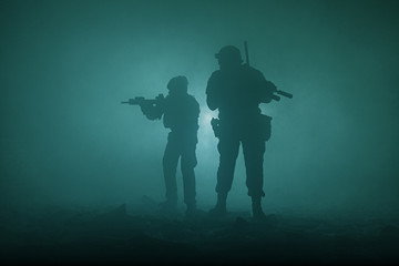 Black silhouettes of pair of soldiers in the smoke haze moving in battle operation. Back light