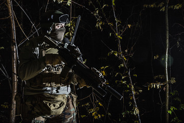 Fototapeta na wymiar Marine Special Operator also known as Marsoc raider with weapons in greenery at nighttime turning looking away. Caucasian, profile view, half length