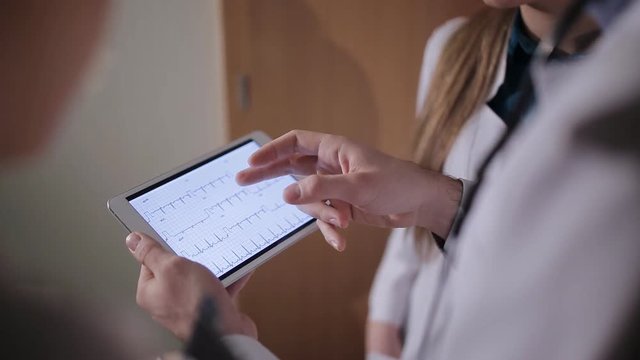 The doctor and two young intern looking at tablet and discuss the results of the patient survey