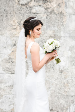 Bride poses with little wedding bouquer before ruined grey wall