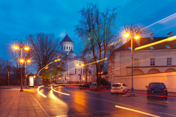 Fototapeta na wymiar Picturesque Street and luminous track from the car at night in Old Town of Vilnius, Lithuania, Baltic states. Our Lady of the Assumption Orthodox Cathedral on the background.