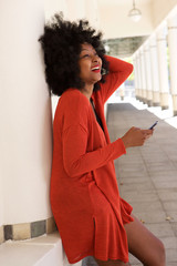 happy african american woman leaning on wall with mobile phone