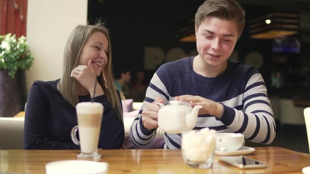 Lovers man and woman laughing in the cute cafe. Loving couple in a cafe. Cup with latte and tea pot on the table.